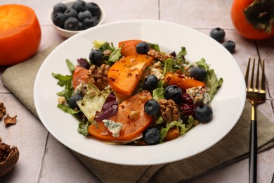 Delicious persimmon salad and fork on tiled surface