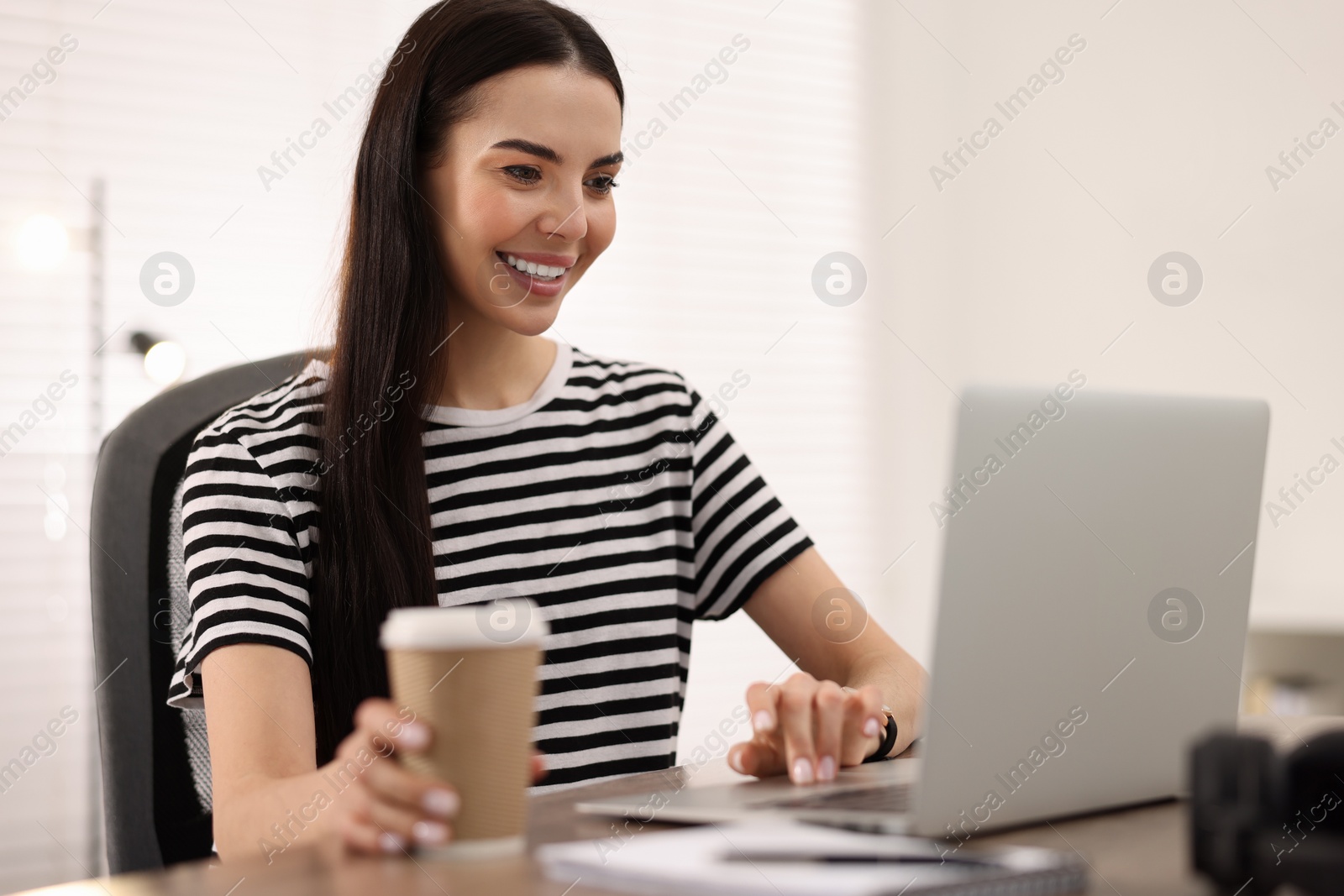 Photo of Young woman watching webinar at table in room