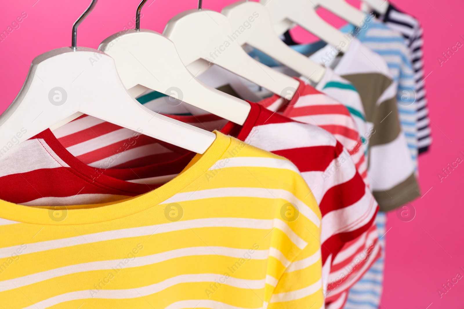 Photo of Colorful clothes on hangers against pink background, closeup