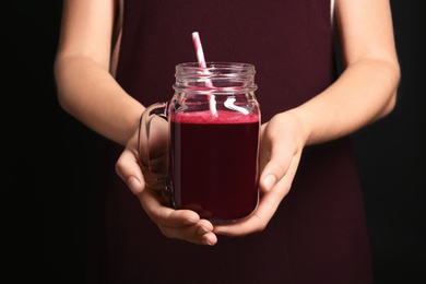 Photo of Woman with mason jar of beet smoothie on black background, closeup