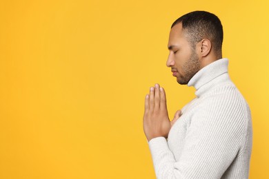 Photo of African American man with clasped hands praying to God on orange background. Space for text