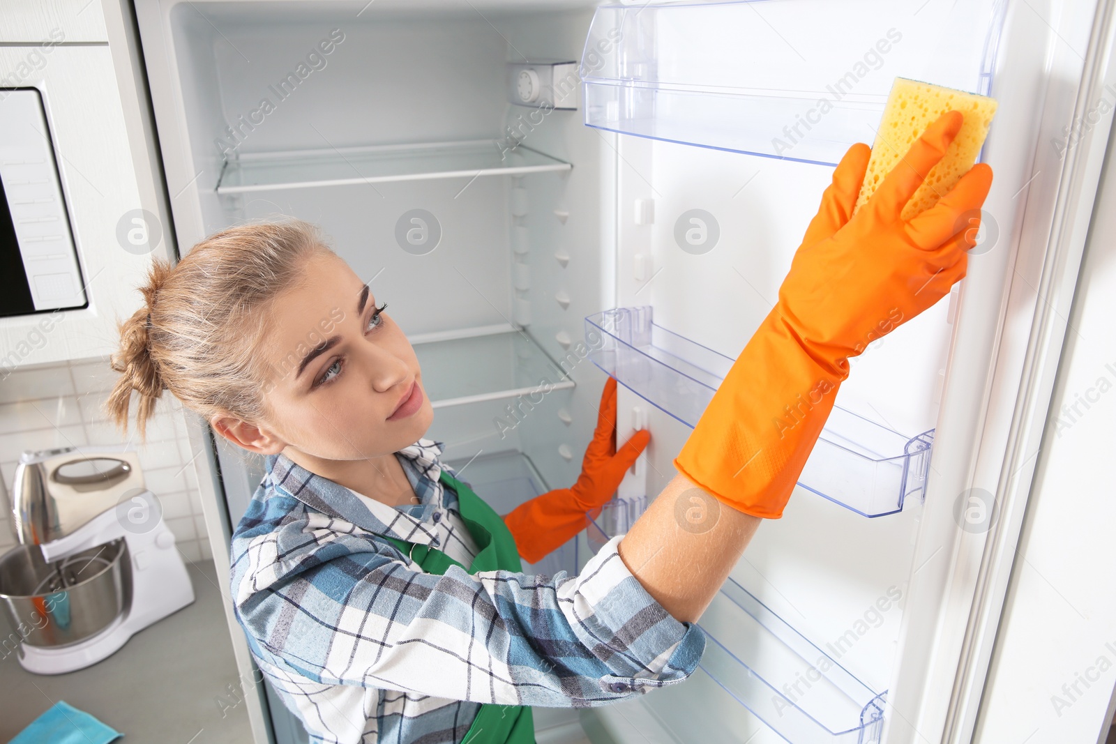 Photo of Woman in rubber gloves cleaning empty refrigerator at home