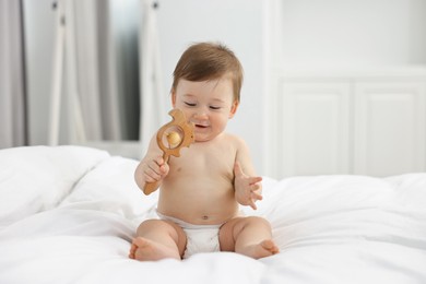 Cute baby boy with wooden rattle on bed at home