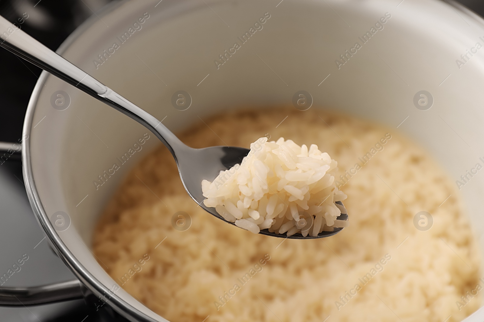 Photo of Wooden spoon with delicious rice over pot, closeup