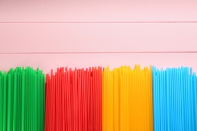 Photo of Colorful plastic drinking straws on pink wooden table, flat lay. Space for text