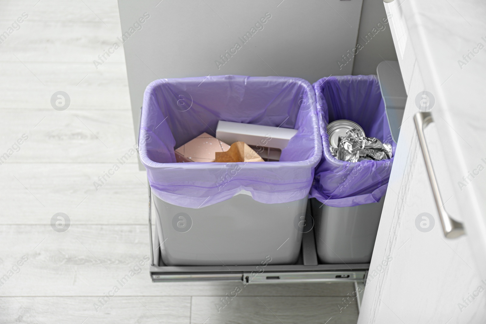 Photo of Open cabinet with full trash bins for separate waste collection in kitchen