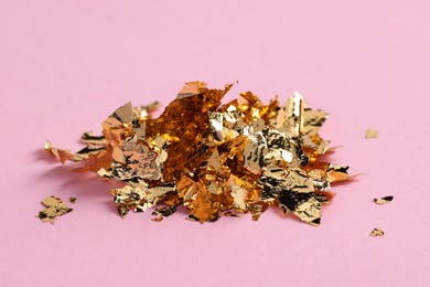 Photo of Pile of edible gold leaf on pink background, closeup