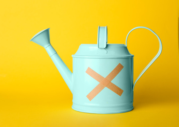 Light blue watering can with sticking plasters on yellow background