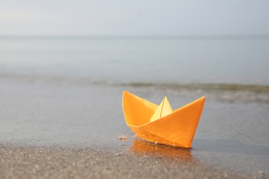 Orange paper boat on sandy beach near sea, space for text