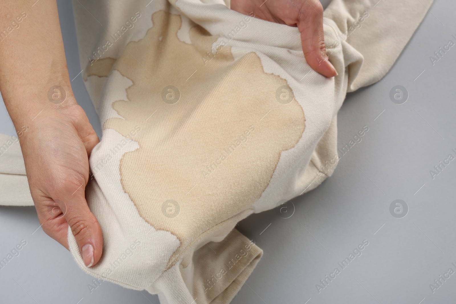 Photo of Woman holding beige sweater with stain on light grey background, closeup