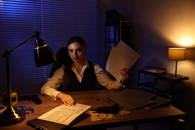 Professional detective working with documents in office at night