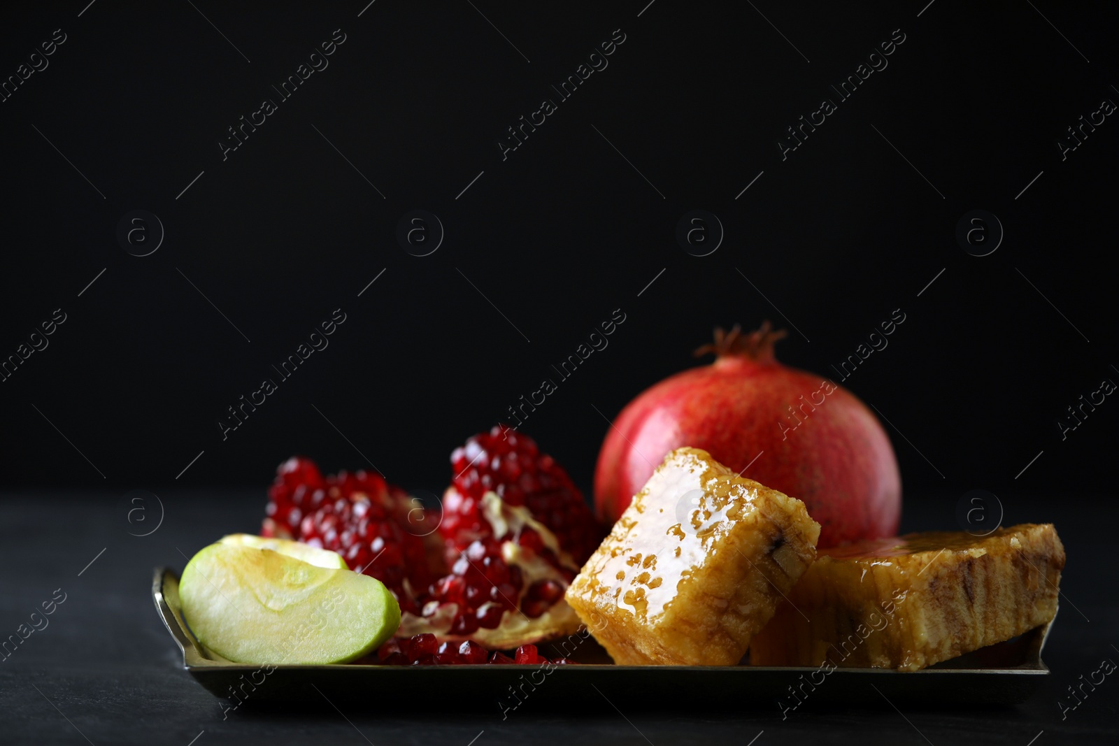 Photo of Honey, apples and pomegranate on dark table. Rosh Hashanah holiday