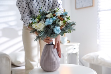 Photo of Woman putting beautiful wedding winter bouquet in vase at home, closeup