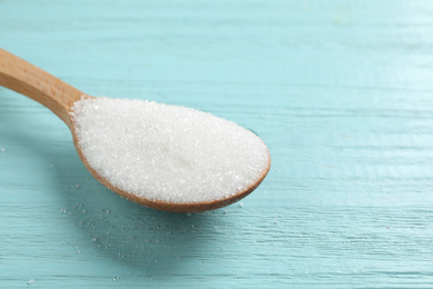 Spoon of white sugar on light blue wooden table, closeup