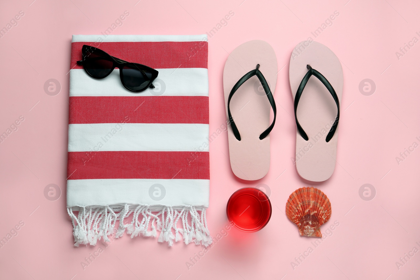 Photo of Beach towel, flip flops and sunglasses on pink background, flat lay