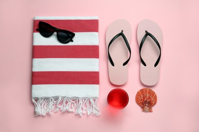 Beach towel, flip flops and sunglasses on pink background, flat lay