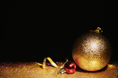 Golden glitter, Christmas balls and streamer against black background. Space for text