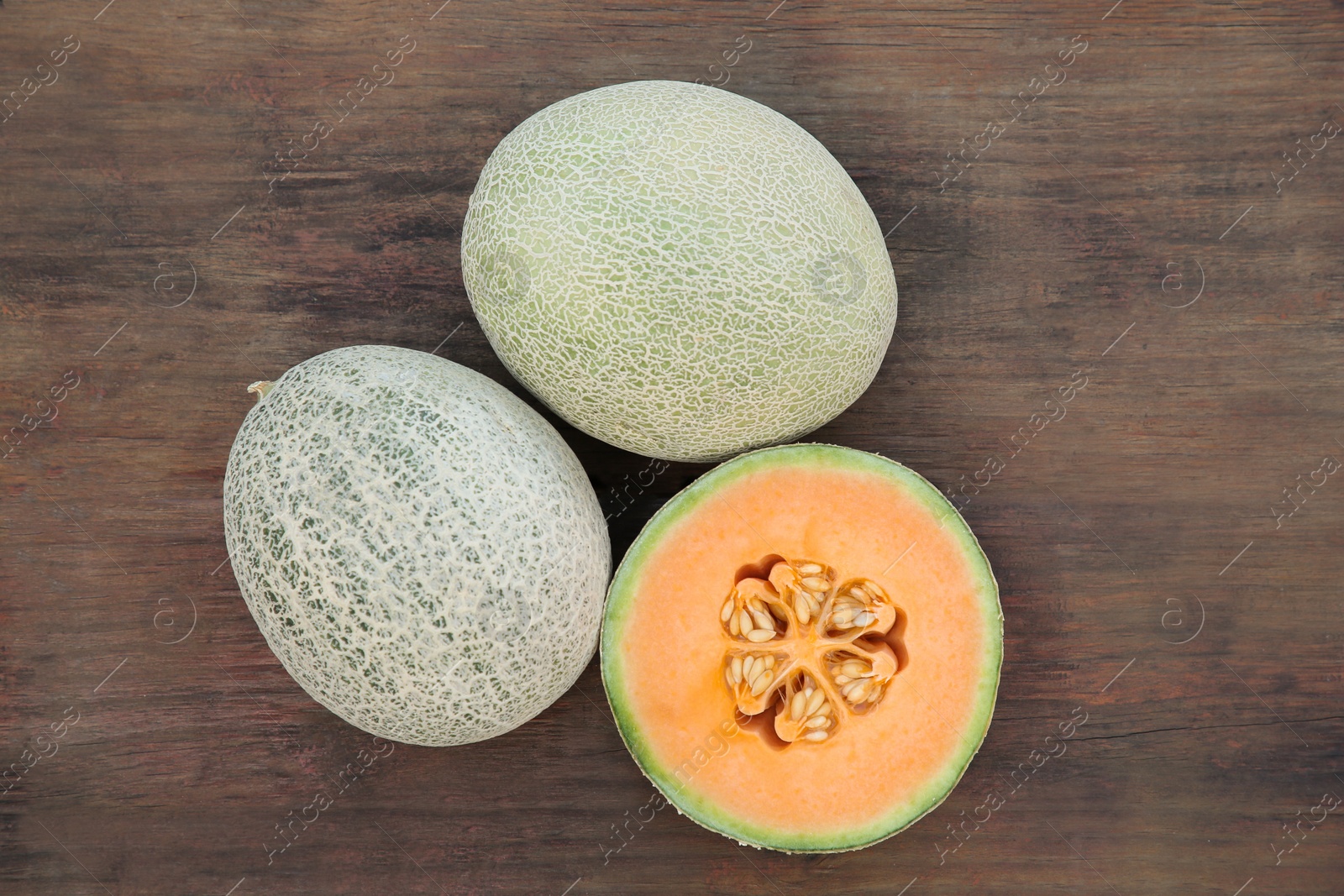 Photo of Whole and cut fresh ripe melons on wooden table, flat lay