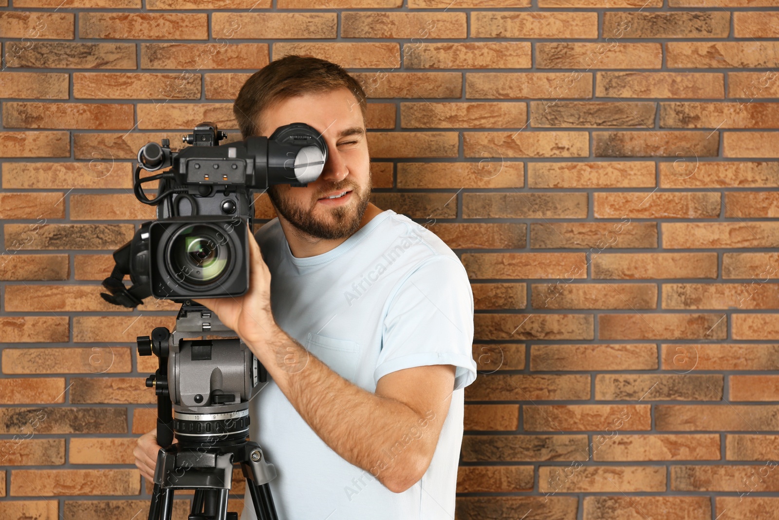 Photo of Operator with professional video camera near brick wall, space for text