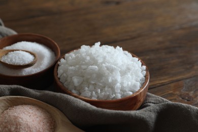 Photo of Different types of organic salt on wooden table, closeup