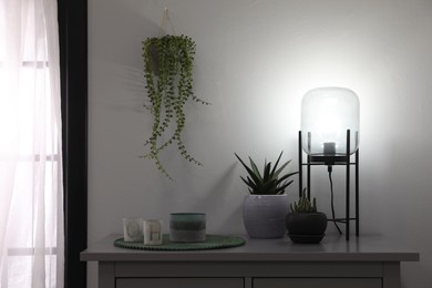 Photo of Stylish lamp, candles and green plants on grey table indoors. Interior design