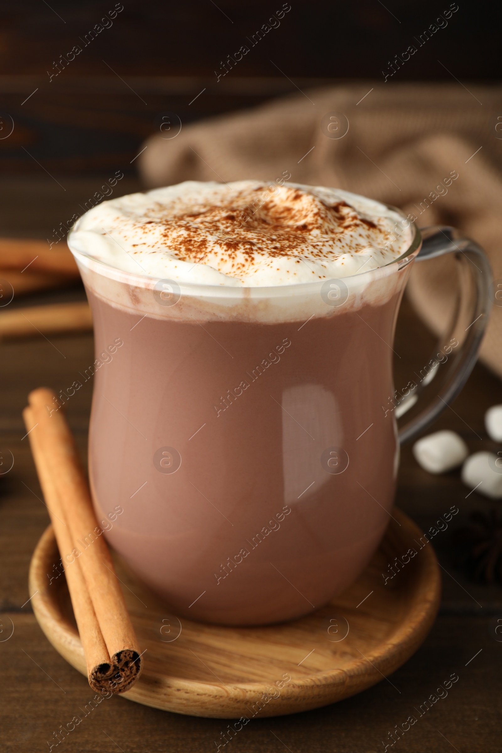 Photo of Glass cup of hot cocoa with whipped cream and aromatic cinnamon on wooden table