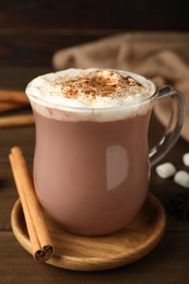 Photo of Glass cup of hot cocoa with whipped cream and aromatic cinnamon on wooden table