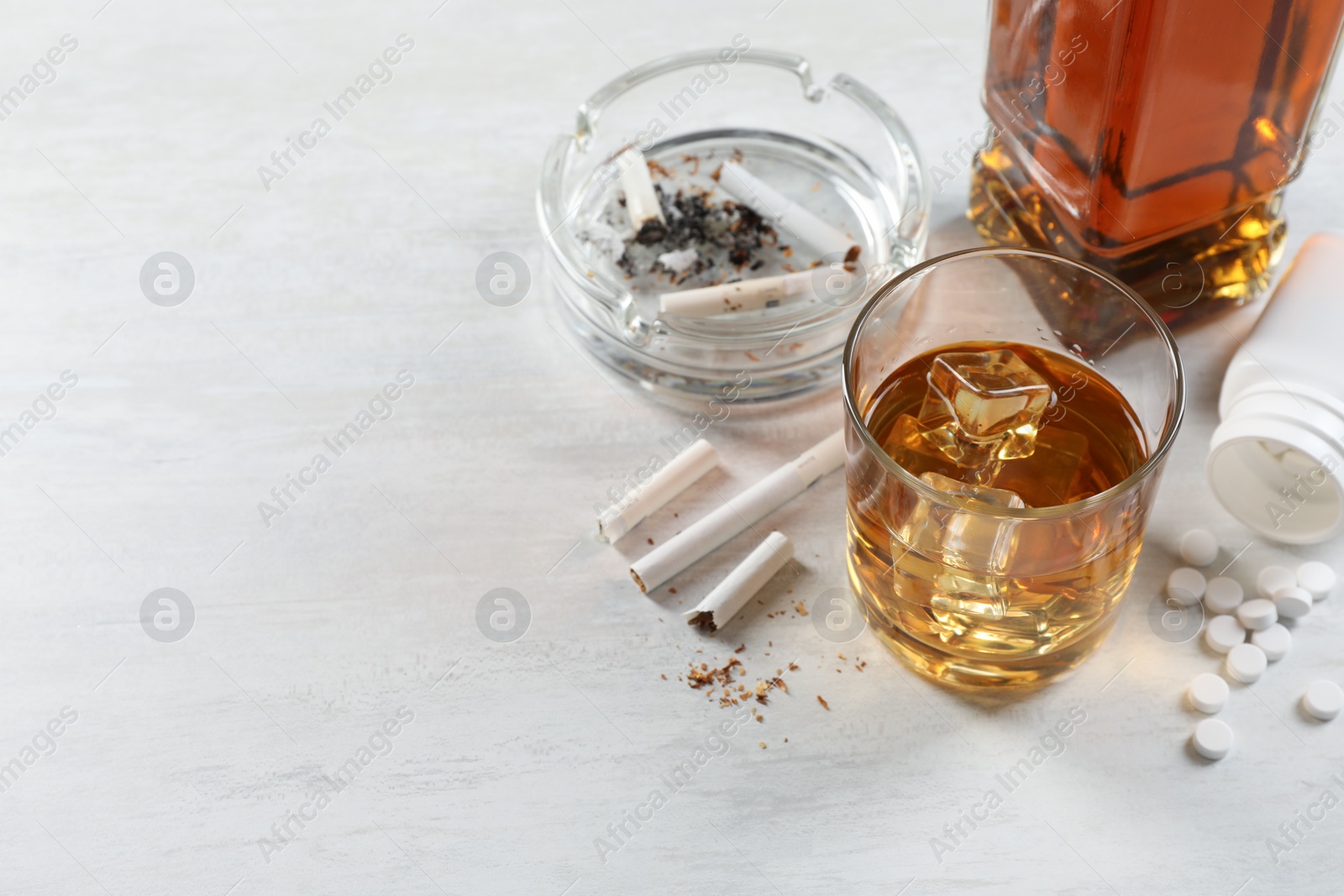 Photo of Alcohol and drug addiction. Whiskey in glass, cigarettes and pills on white table, space for text