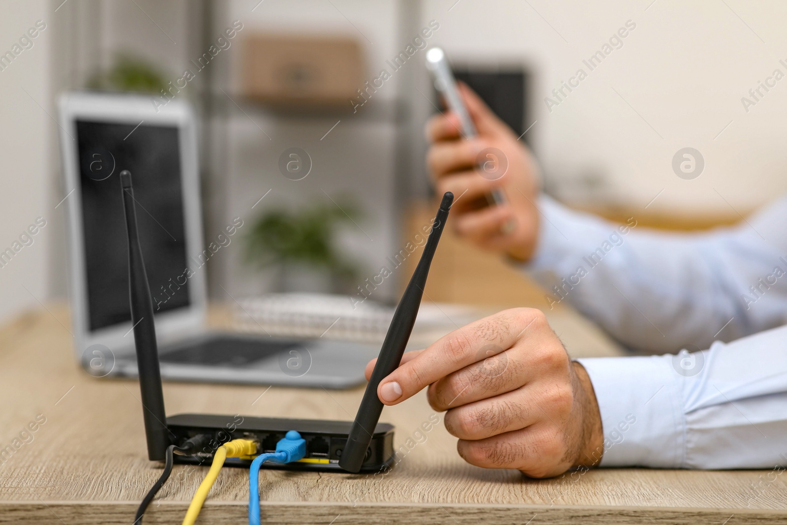 Photo of Man with smartphone and laptop connecting to internet via Wi-Fi router at wooden table, closeup