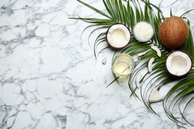 Jug of natural organic oil and coconuts on marble background, flat lay. Space for text