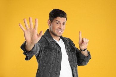 Photo of Man showing number six with his hands on yellow background