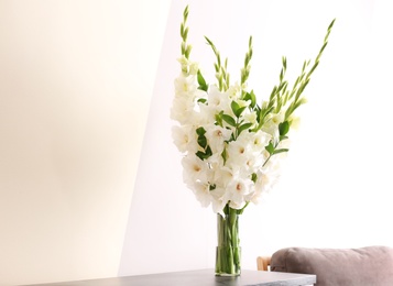 Photo of Vase with beautiful white gladiolus flowers on wooden table near color wall. Space for text