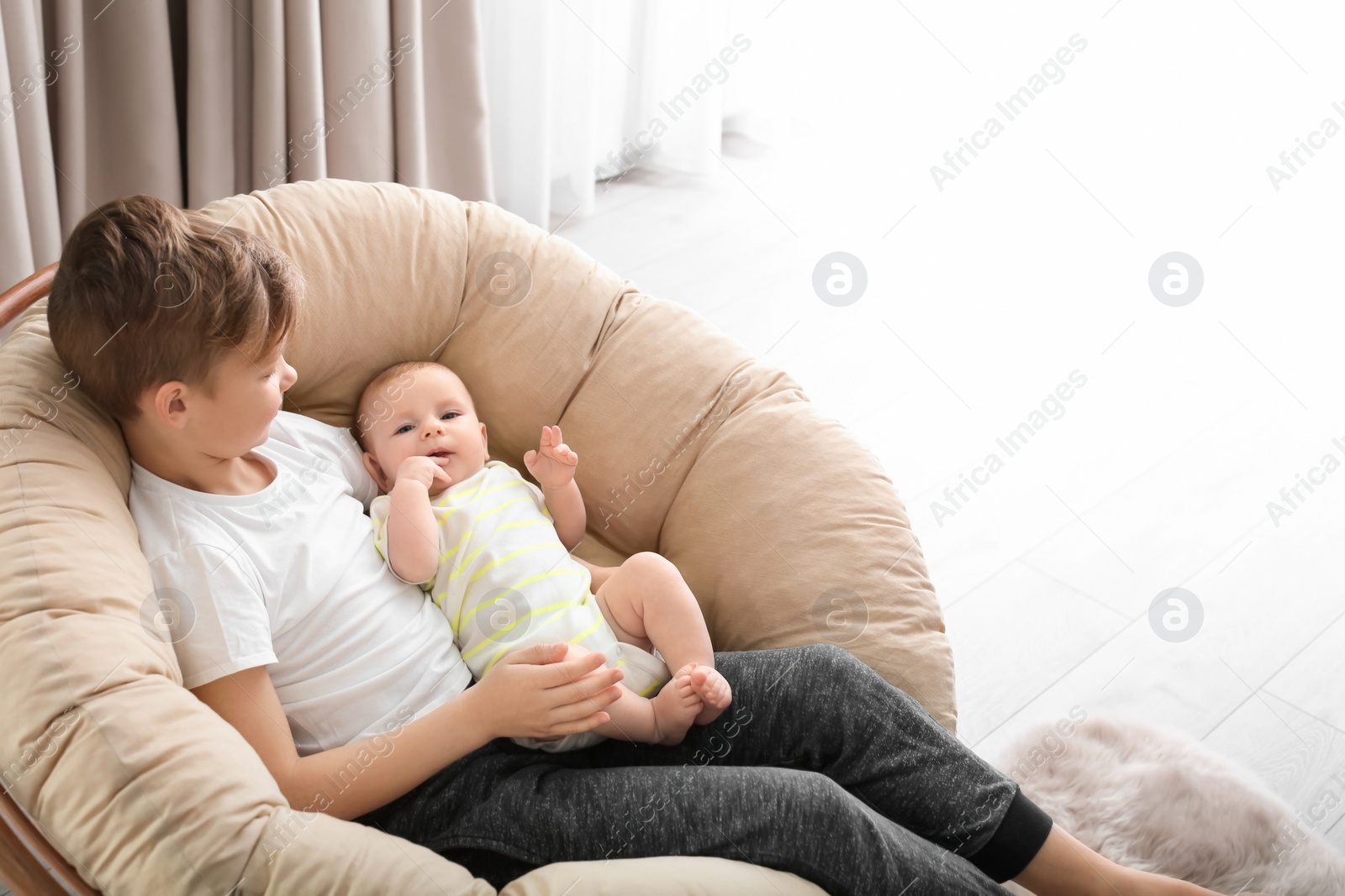 Photo of Cute boy with little baby in lounge chair at home