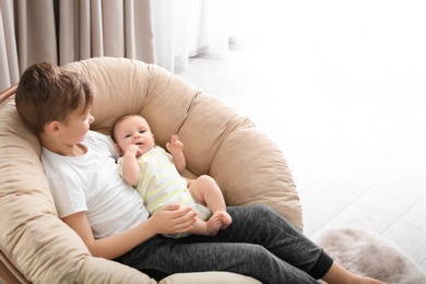 Photo of Cute boy with little baby in lounge chair at home