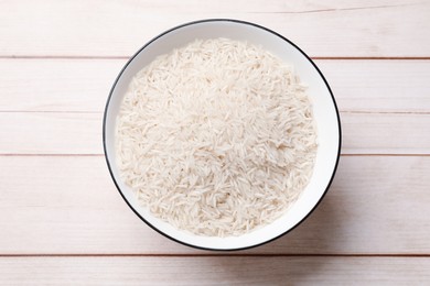 Photo of Raw basmati rice in bowl on white wooden table, top view