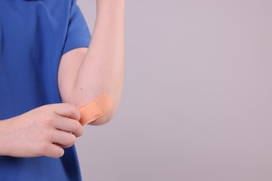 Little boy putting sticking plaster onto elbow against light grey background, closeup. Space for text