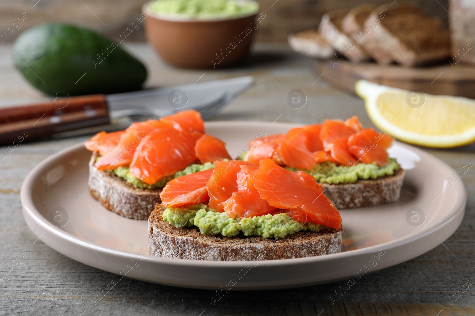 Photo of Delicious sandwiches with salmon and avocado on grey wooden table, closeup