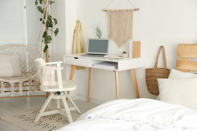 Stylish room interior with workplace, hanging chair and bed