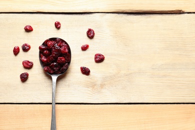 Photo of Spoon of cranberries on wooden background, top view with space for text. Dried fruit as healthy snack