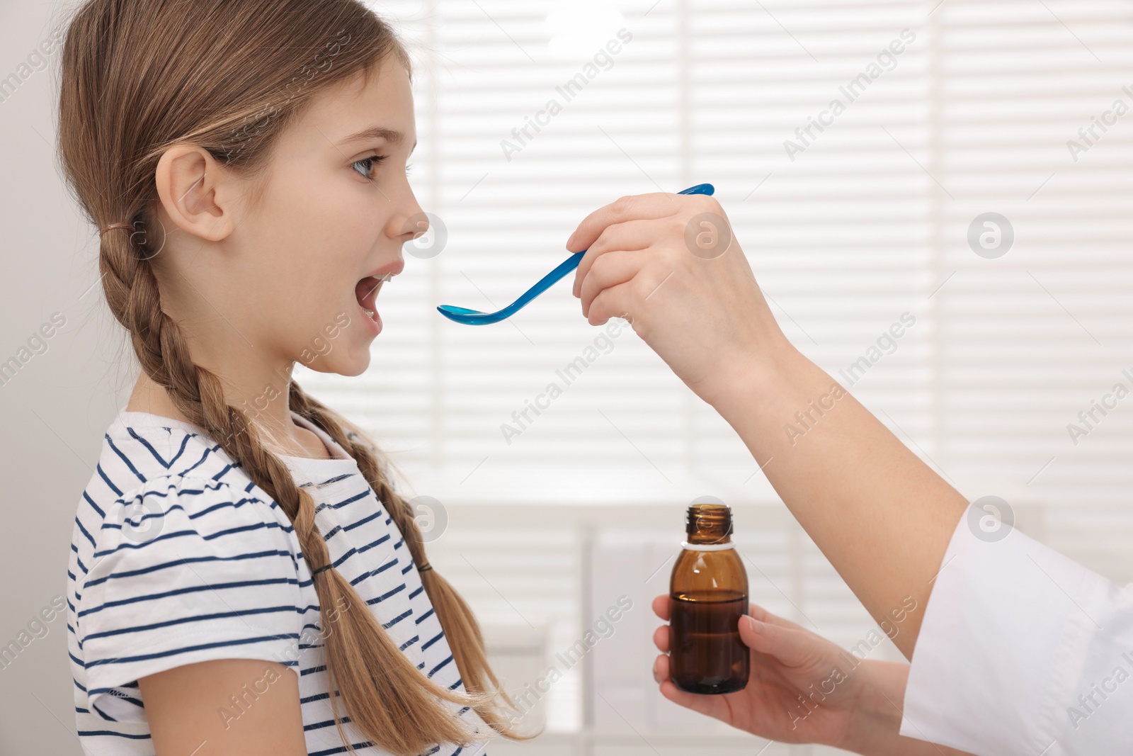 Photo of Doctor giving cough syrup to girl in clinic