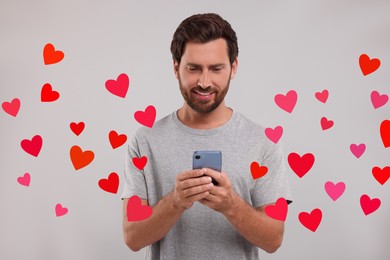 Long distance love. Man chatting with sweetheart via smartphone on grey background. Hearts flying out of device and swirling around him
