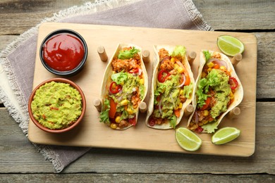 Delicious tacos with guacamole, meat and vegetables served on wooden table, top view