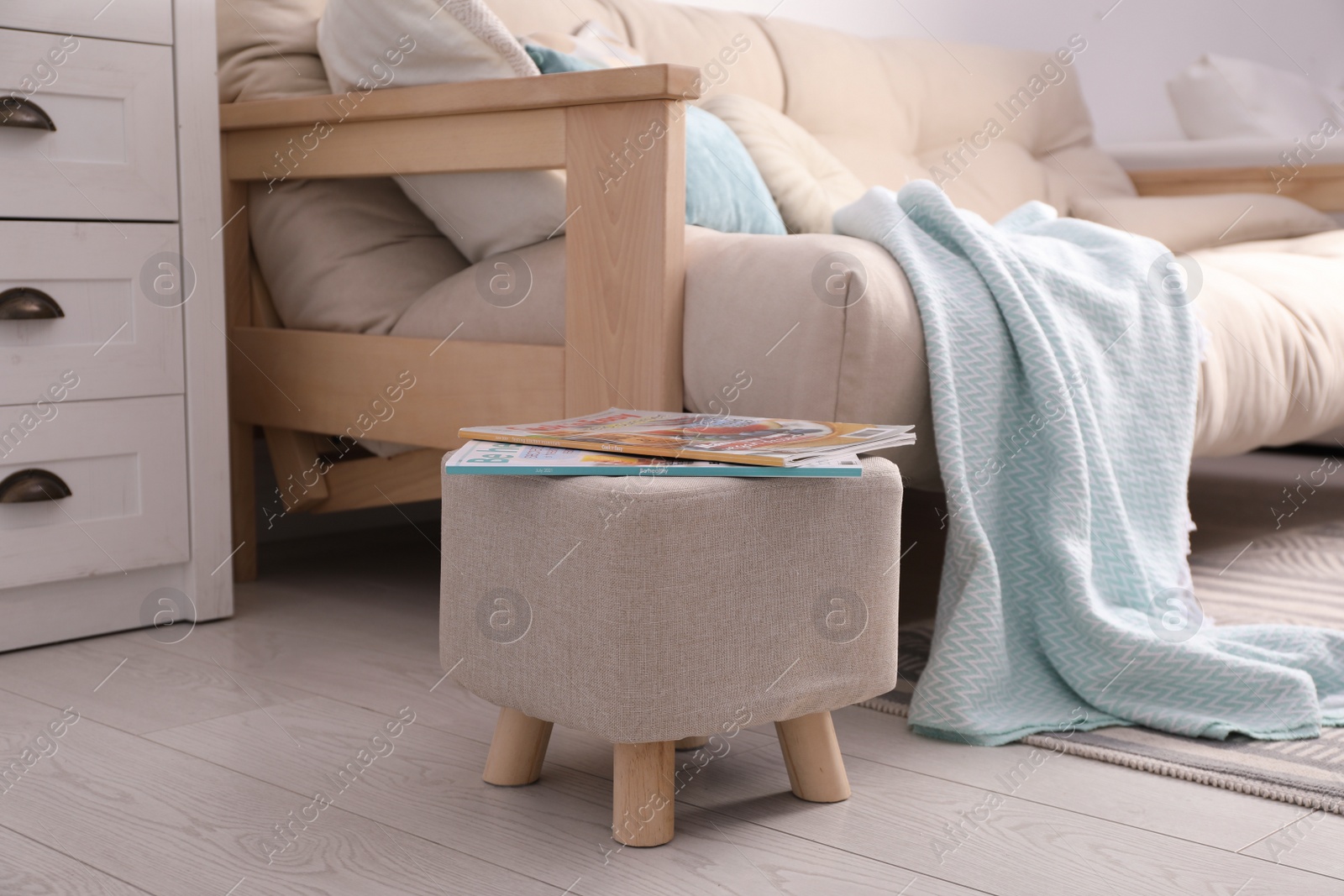 Photo of Stylish ottoman with magazines near sofa in light living room