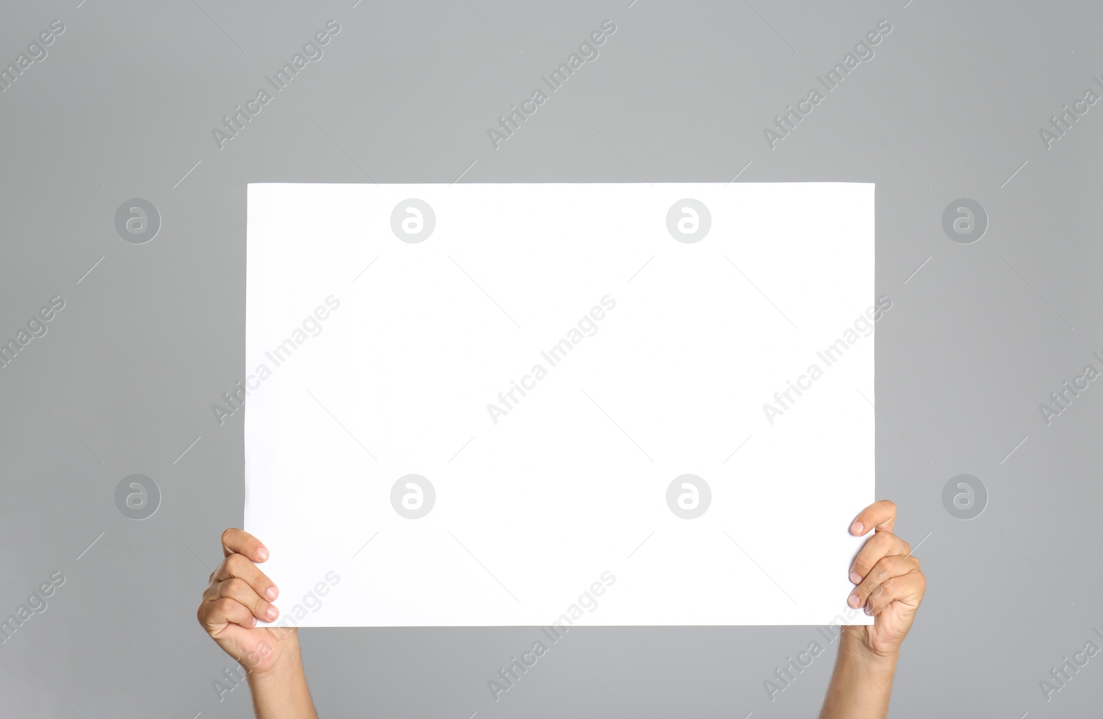 Photo of Man holding white blank poster on grey background, closeup. Mockup for design