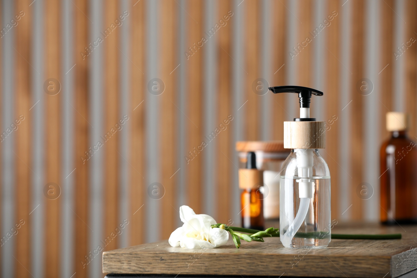 Photo of Bottle with dispenser cap and beautiful flower on wooden table indoors. Space for text