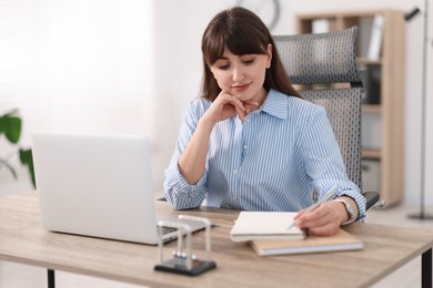 Photo of Woman taking notes during webinar at wooden table indoors