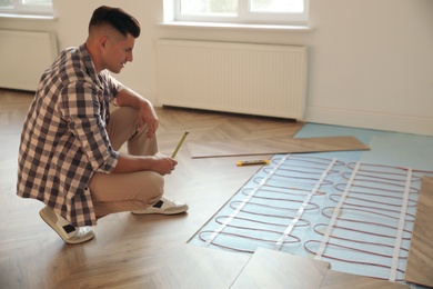 Photo of Professional worker installing electric underfloor heating system indoors