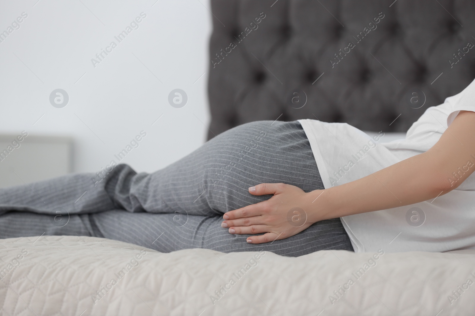 Photo of Young woman suffering from hemorrhoid on bed at home, closeup