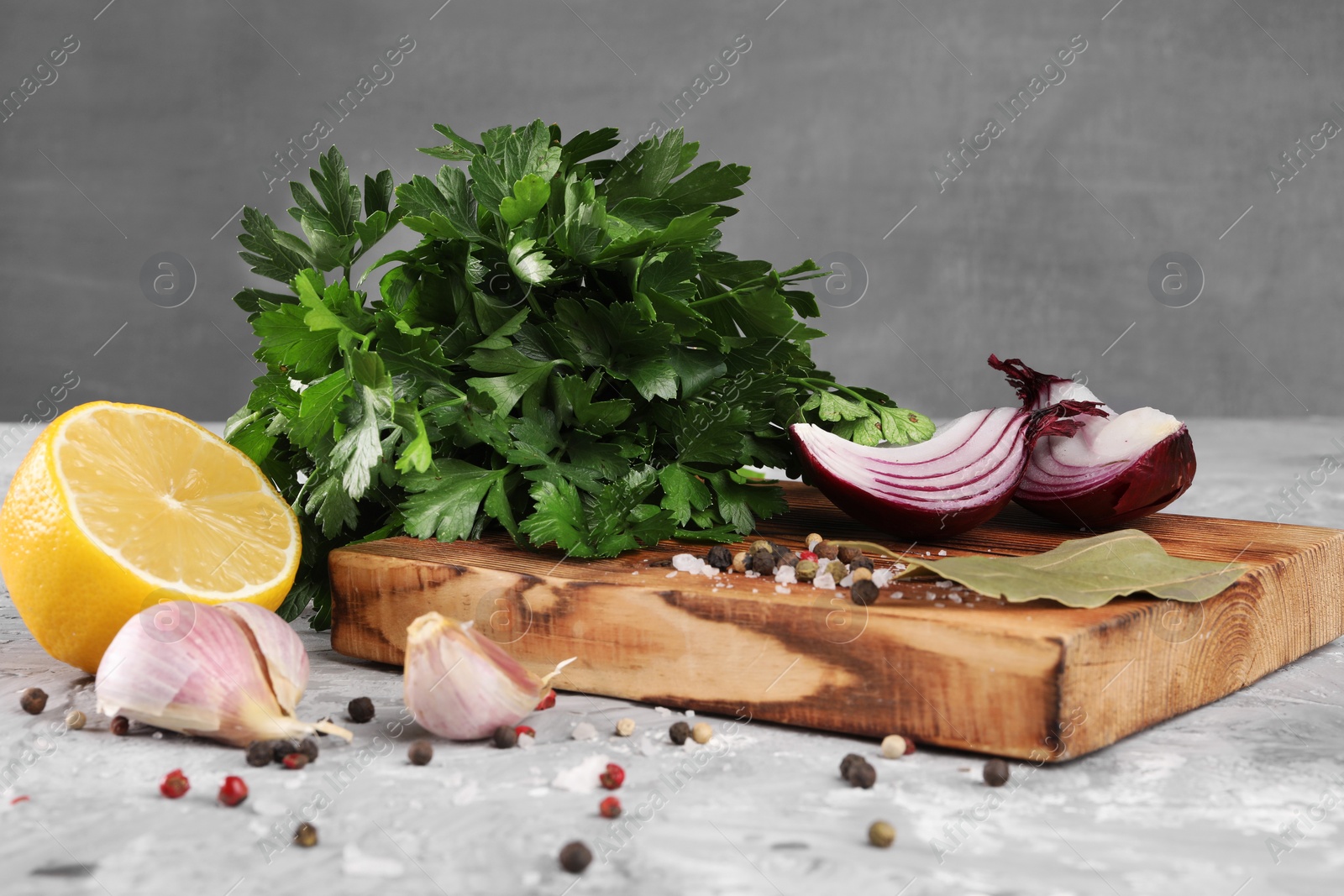 Photo of Bunch of fresh parsley, lemon, onion, garlic and spices on grey textured table