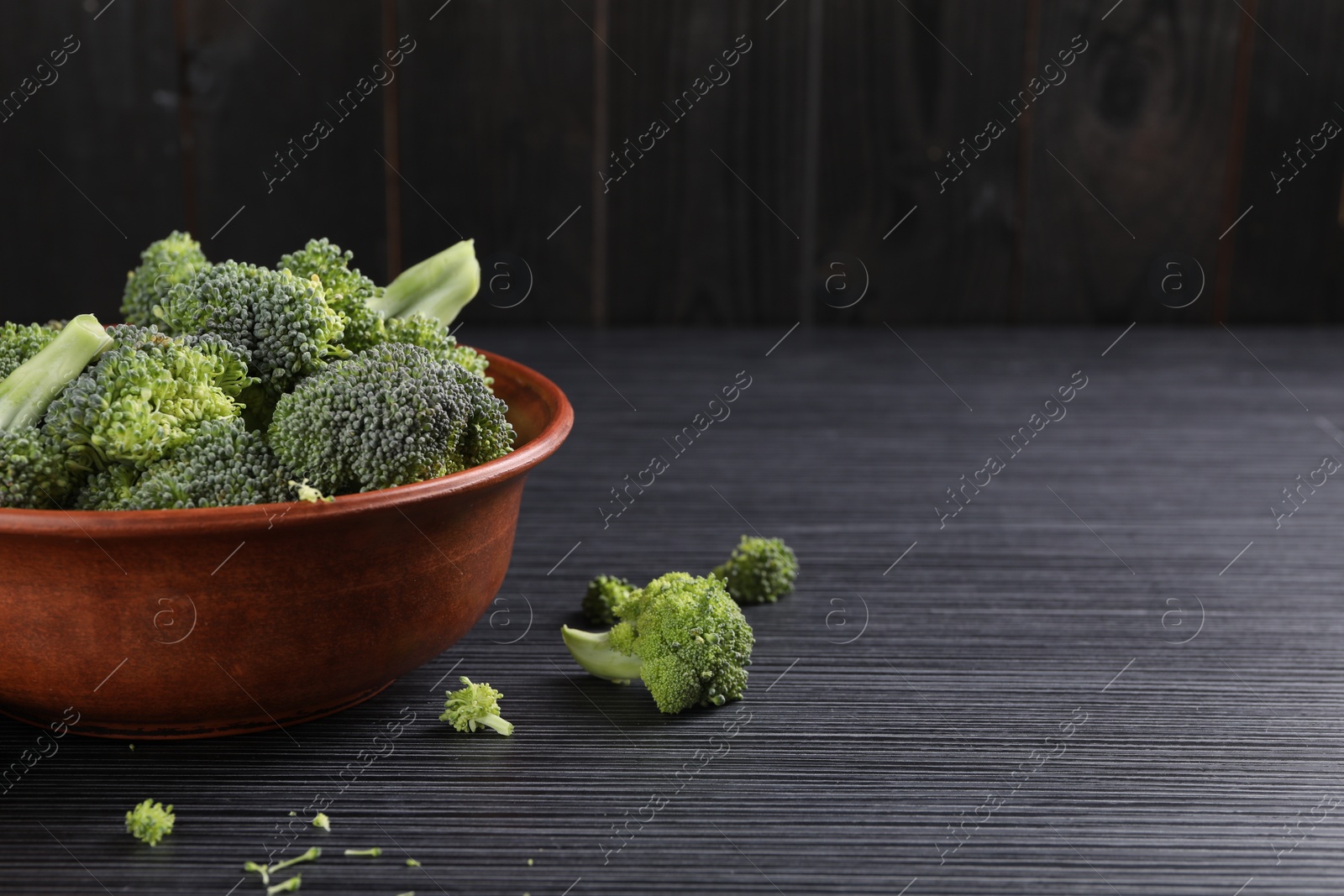 Photo of Bowl with fresh raw broccoli on black wooden table, closeup. Space for text